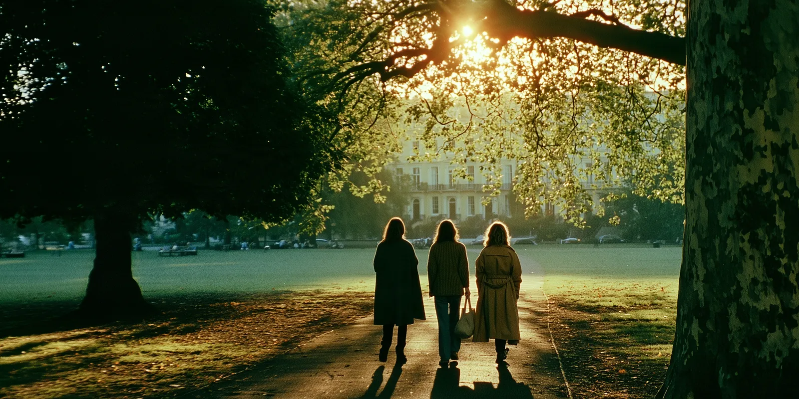 Three women walking together along a tree-lined park path in warm afternoon light