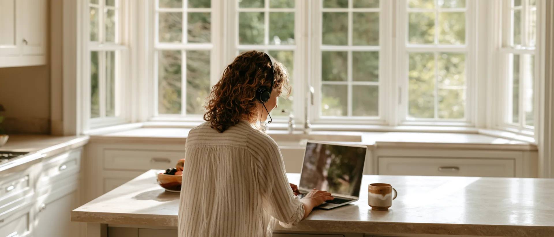 A woman with a headset in a live video session at a bright kitchen counter