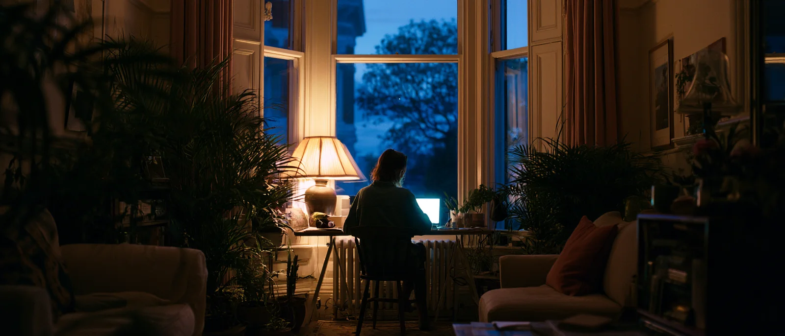 A dim living room in the evening, a lamp glowing